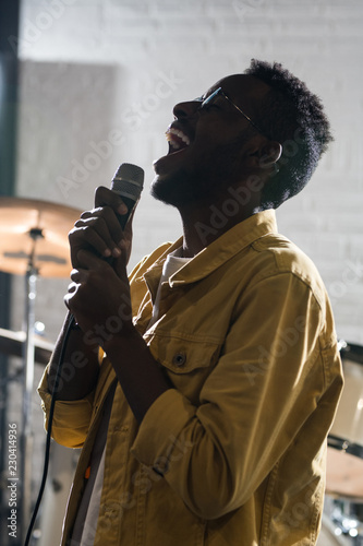 Side view backlit portrait of inspired African-American man singing to microphone while performing on stage