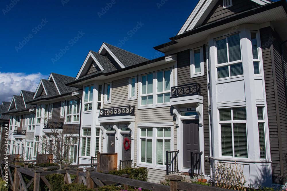 Row of new townhomes in a sidewalk neighborhood. On a sunny day in spring against bright blue sky.