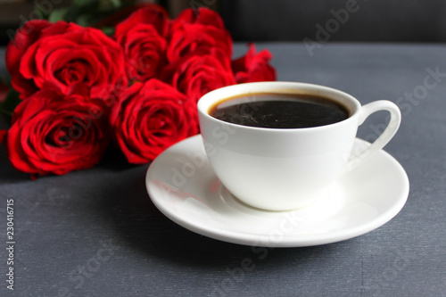 Black coffee in a white Cup with a saucer on the table, a bouquet of red roses. Cafe, restaurant, coffee with your loved one, a beautiful bouquet.Top view