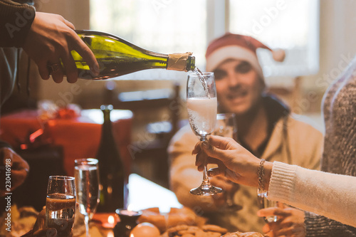 Group of friends celebrating Christmas, preparing flutes with champaign, pouring sparkling wine