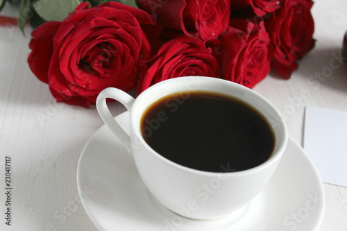 Black coffee in a white Cup with a saucer on the table, a bouquet of red roses. Cafe, restaurant, coffee with your loved one, a beautiful bouquet.Top view