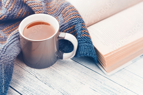 Cup of tea, book and knitted scarf on wooden background