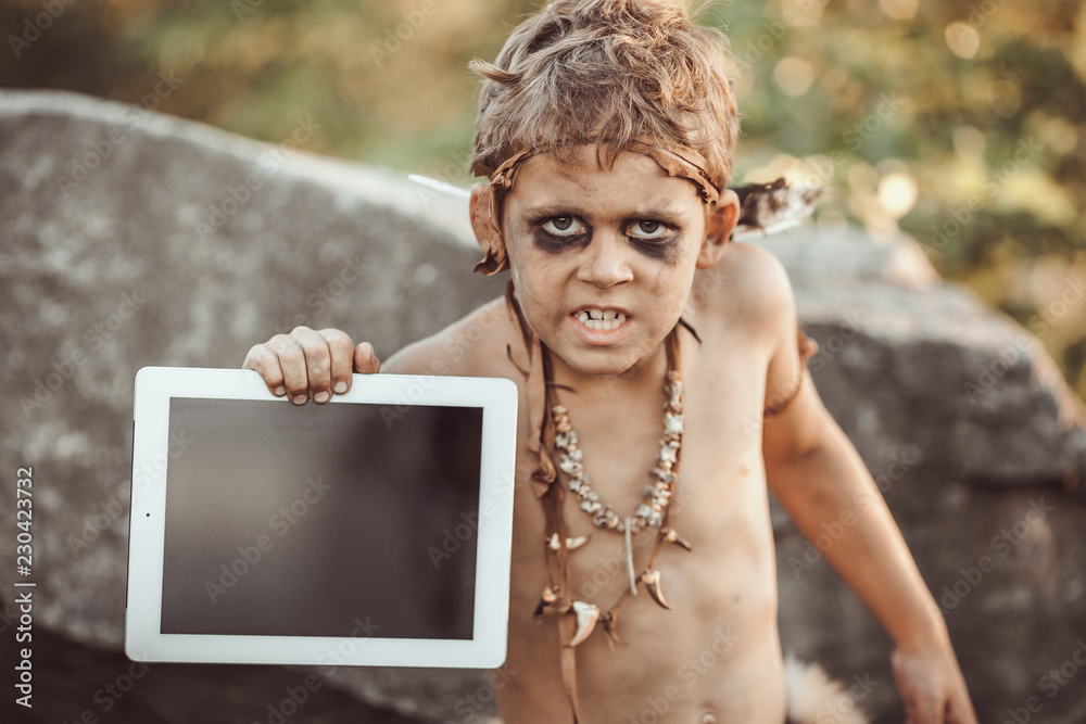 Caveman, manly boy holding tablet PC. Funny young primitive boy outdoors.  Evolution degradation concept. Calm boy outside against rocky background.  Prehistoric tribal man outside on wild nature with Stock Photo | Adobe