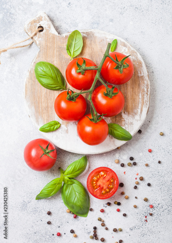 Organic Cherry Tomatoes on the Vine with basil and pepper on chopping board on stone kitchen background.