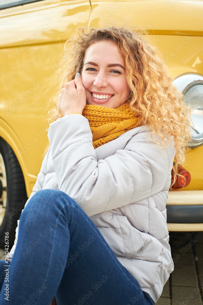 Portrait of young attractive redhead curly girl siting front of yellow van and smiling