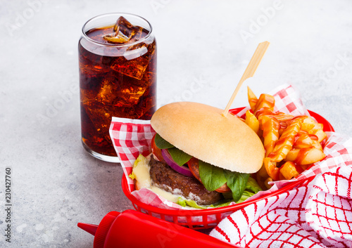 Fresh beef burger with sauce and vegetables and glass of cola soft drink with potato chips fries in red serving basket on stone kitchen table background. photo