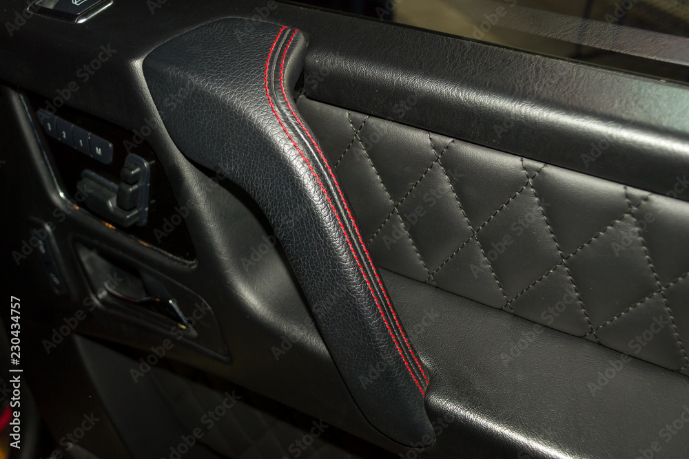 A view of a part of the interior of the car door from leather of black color, stitched double thread of red color with contrast stitching in a vehicle interior design workshop