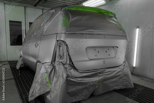 Full painting of a silver car in the back of a hatchback, some parts of which are protected by paper from splashes of paint droplets in a car body repair shop with a special box and equipment