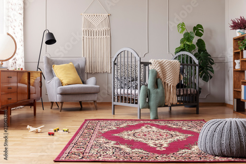 Rustic rug in stylish baby bedroom with grey and vintage furniture, real photo with copy space photo