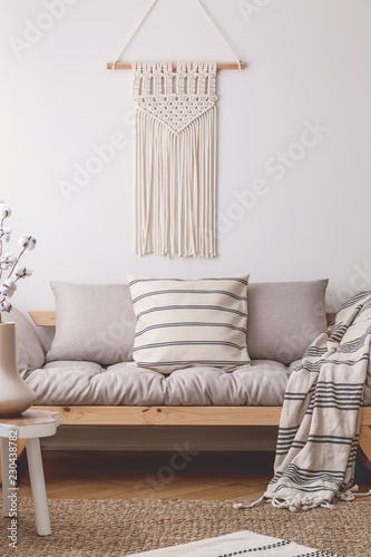 White handmade macrame above comfortable beige living room sofa with lot of pillows and blanket with stripes