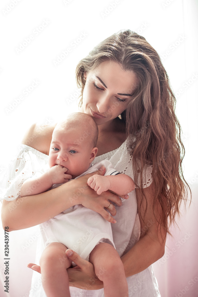 Beautiful young mother holds the baby in her arms. Mom holds the baby's legs in her hands for 3 months. Love. Motherhood. Happiness. House. Cozy. Beautiful young mother holds the baby in her arms. Mom holds the baby's legs in her hands for 3 months. Love. Motherhood. Happiness. House. Cozy.