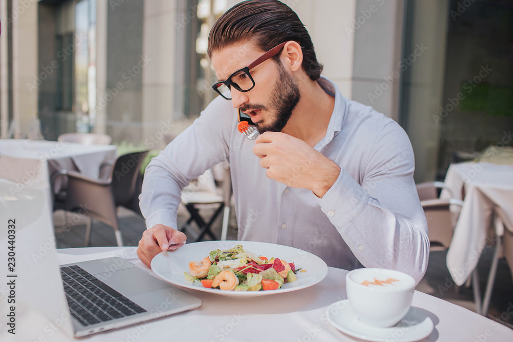 Busy man answers phone call during lunch. He talks and holds plate with salad at the same time. There are cup of coffee as well. Busy man answers phone call during lunch. He talks and holds plate with salad at the same time. There are cup of coffee as well.