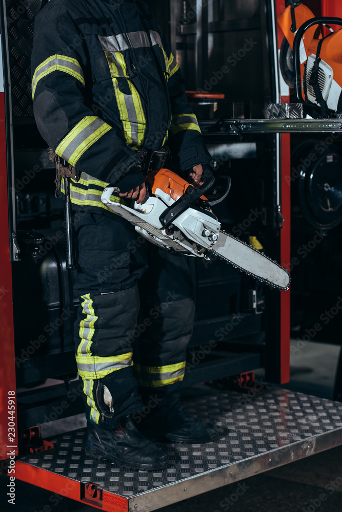partial view of firefighter in protective uniform holding electric saw in hands at fire station partial view of firefighter in protective uniform holding electric saw in hands at fire station