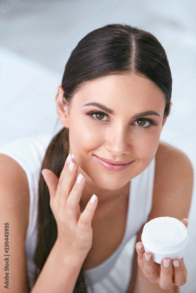 Woman Applying Facial Cream On Face Skin In White Interior