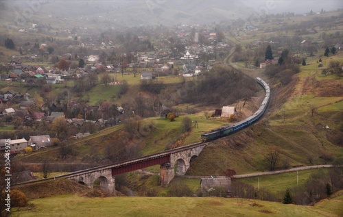 Obraz na płótnie Train Rides On A Winding Railway. Autumn Rural Landscape With Locomotive, Railway Viaduct, Mountains And A Village Located On The Slopes Of The Mountains. Transcarpathia, The Border Of Western Ukraine w salonie