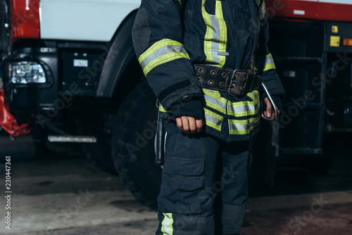 partial view of firefighter in protective fireproof uniform standing at fire department