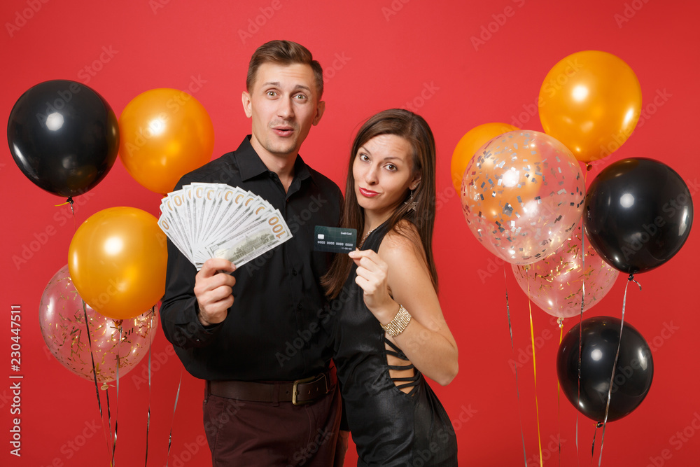 Fototapeta premium Fun couple celebrating birthday holiday party hold lot cash money, credit card isolated on bright red background air balloons St. Valentine International Women Day Happy New Year 2019 concept. Mock up