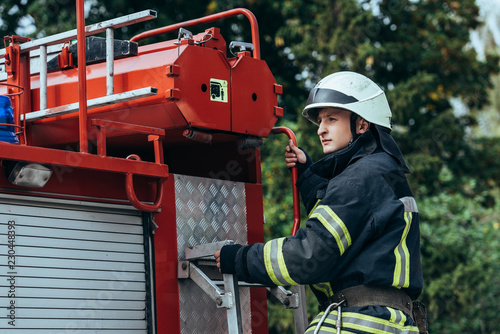 male firefighter in protective helmet standing on truck on street
