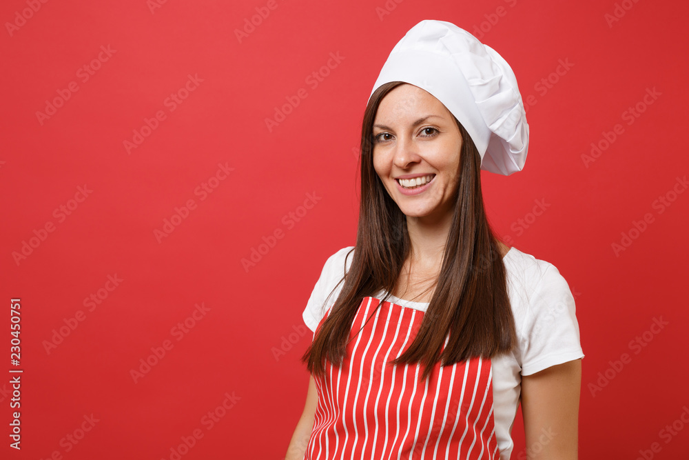 Housewife female chef cook or baker in red striped apron, white t-shirt, toque chefs hat isolated on red wall background. Close up portrait of housekeeper brunette woman. Mock up copy space concept. Housewife female chef cook or baker in red striped apron, white t-shirt, toque chefs hat isolated on red wall background. Close up portrait of housekeeper brunette woman. Mock up copy space concept.