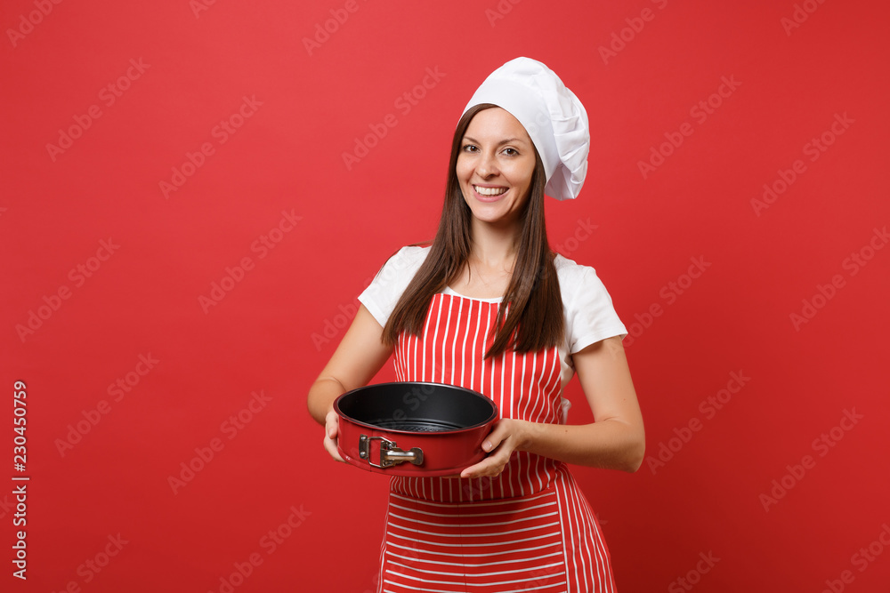 Housewife female chef cook or baker in striped apron, white t-shirt, toque chefs hat isolated on red wall background. Housekeeper woman holding metal baking form for pie. Mock up copy space concept. Housewife female chef cook or baker in striped apron, white t-shirt, toque chefs hat isolated on red wall background. Housekeeper woman holding metal baking form for pie. Mock up copy space concept.