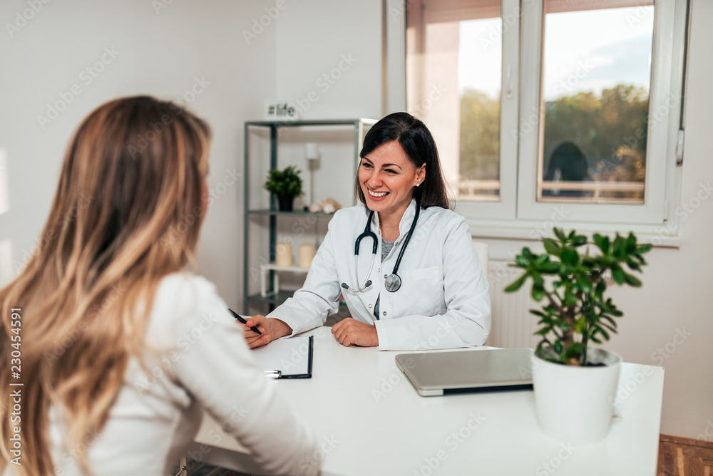 Behang Beautiful young female doctor smiling while talking to her patient