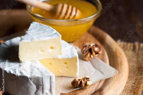 Brie type of cheese. Camembert cheese. Fresh Brie cheese and a slice on a wooden board with nuts, honey and leaves. Italian, French cheese.