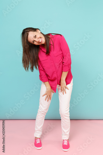 Full length portrait of smiling young pretty woman in rose shirt blouse, white pants posing isolated on bright pink blue pastel wall background studio. Fashion lifestyle concept. Mock up copy space.