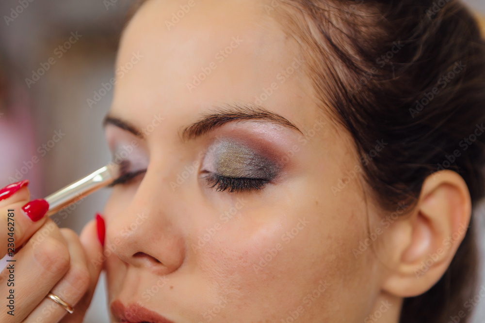 Make-up artist doing make up to the model in studio.