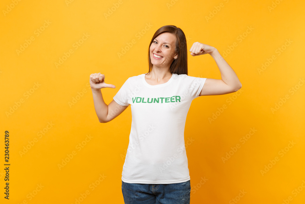 Portrait of happy smiling satisfied woman in white t-shirt with written inscription green title volunteer isolated on yellow background. Voluntary free assistance help, charity grace work concept.