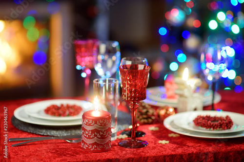 Beautiful table setting for Christmas party or New Year celebration at home. Cozy room with a fireplace and Christmas tree in a background.