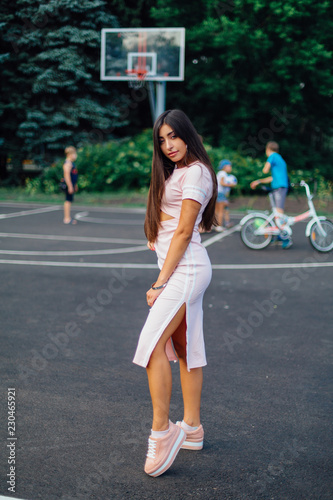 Charming brunette female dressed in a pink dress posing on the basketball court.