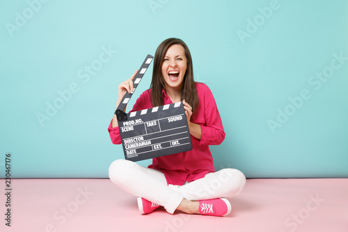 Photo Full length shot woman in rose shirt white pants sitting on floor with film making clapperboard isolated on bright pink blue pastel wall background studio