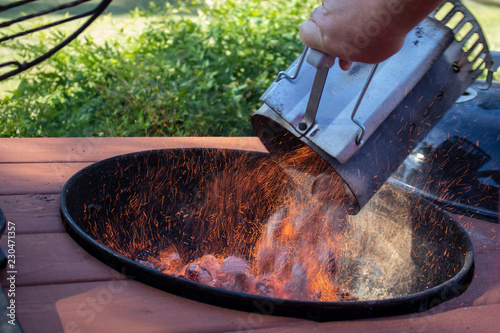 Bbq chimney charcoal fire starter full of burning briquettes being dumped into an outdoor grill with sparks flying photo