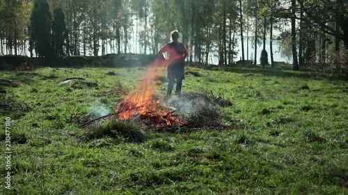 Bonfire in autumn. Bonfire on a meadow to get rid of old bushwood. Woman throwing old branches and leaves on fire. Rural settings in the south of Sweden. photo