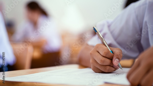 Close-up hand of students writing an exam in classroom