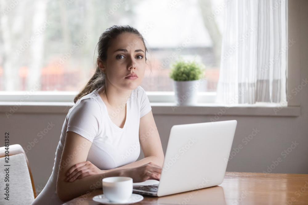 Worried young millennial woman sitting in kitchen at table having problems looking at camera at home. Pensive beautiful female use computer device received bad news feels stressed unhappy and upset Worried young millennial woman sitting in kitchen at table having problems looking at camera at home. Pensive beautiful female use computer device received bad news feels stressed unhappy and upset