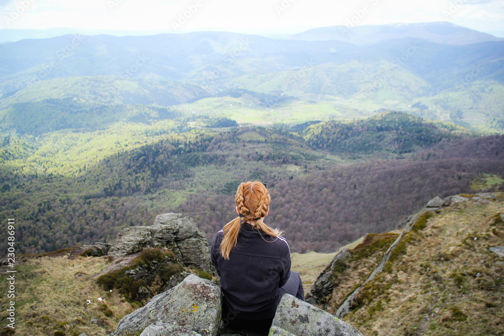 Naklejka premium The girl sits on the edge of a cliff with a view of the mountains. Ukrainian Carpathian Mountains. Traveling