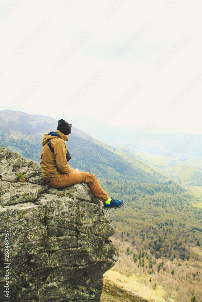 Fototapeta premium The girl sits on the edge of a cliff with a view of the mountains. Ukrainian Carpathian Mountains. Traveling