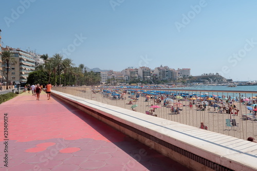 Paseo de la playa de Poniente de Benidorm en España con gente irreconocible paseando, tomando el sol en la arena y bañandose en el agua