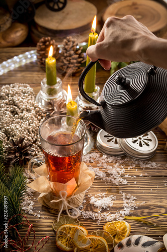 Process of pouring tea into the glass cup on wooden table on christmas decorated background
