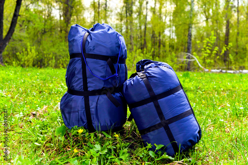 Sleeping tourist bags blue, rolled up in the forest on a background of grass.