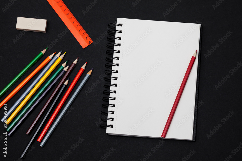 Modern black office desk table with colorful pencils and blank notebook page for input the text. Top view, flat lay Modern black office desk table with colorful pencils and blank notebook page for input the text. Top view, flat lay