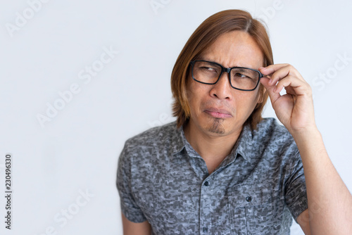 Nerdy Asian guy fooling at camera. Closeup of young man in casual touching eyeglasses, looking away and grimacing. Crazy face concept