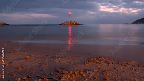 Lighthouse shining on an island on the shore of the beach with the reflection of light in the water at sunset on a cloudy day in Benidorm, Spain