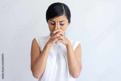 Tired Korean girl suffering from headache. Young Asian woman in white sleeveless shirt closing eyes and leaning head on fingers. Headache or fatigue concept