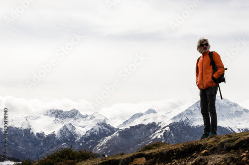 Man in orange jacket and backpack and camera, doing trekking along a hill with herbs. In the background the peak of Peña Rueda. Cold weather, snow in the hills. Winter hiking. Asturias, Spain, Europe