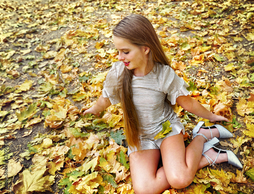 Autumn fashion child silver metalic mini party dress with short sleeve in princess style. Top view of girl sitting on fall leaves in city park outdoor.