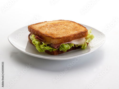 Sandwich de jamón y queso con lechuga dentro de un plato ovalado blanco, sobre fondo blanco