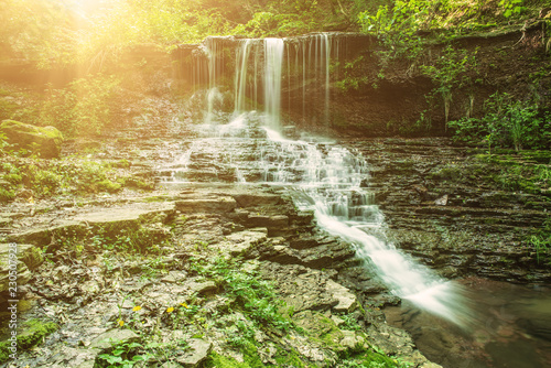 Beautiful mountain rainforest waterfall with fast flowing water and rocks, long exposure. Natural seasonal travel outdoor background with sun shihing photo