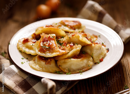 Fried dumplings stuffed with cabbage and meat sprinkled with bacon greaves and chopped parsley on a white plate on a wooden rustic table. photo